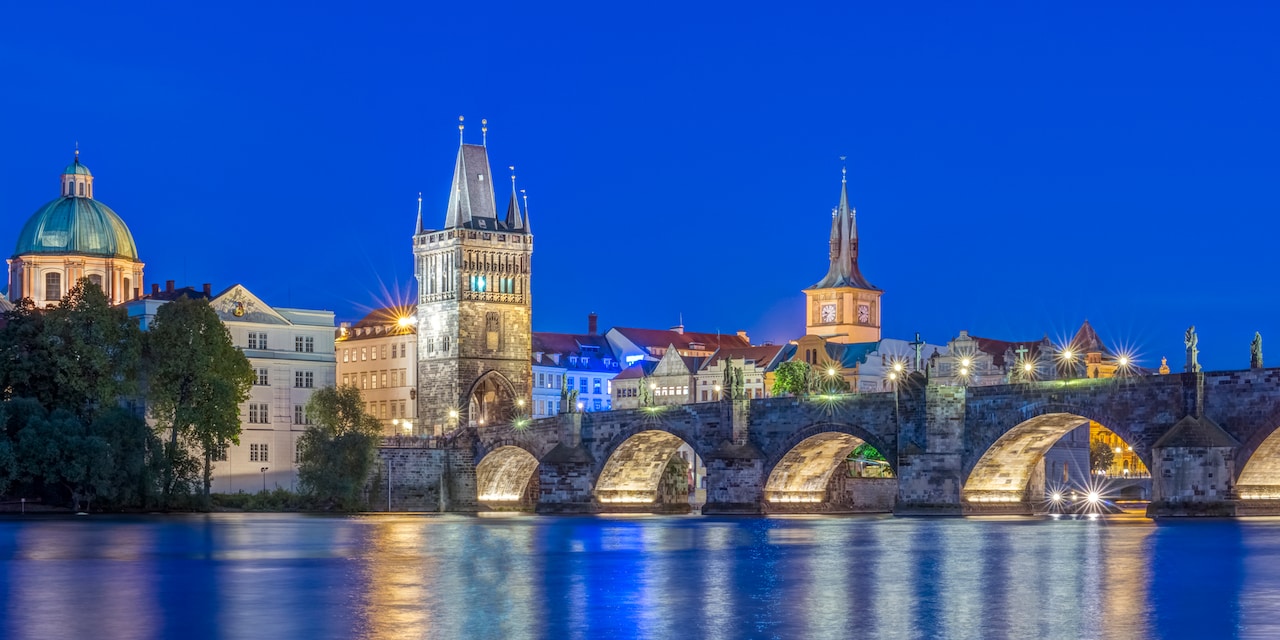 A nighttime image of an illuminated Charles Bridge spanning the Vltava River in Prague, Czech Republic