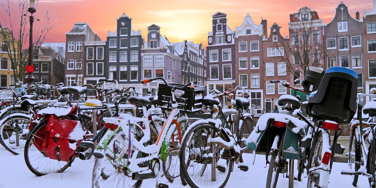 A group of snow covered bicycles parked near a row of buildings in Amsterdam