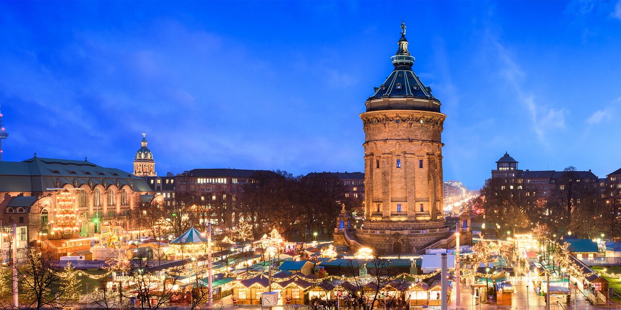 A Christmas market lit up at night near the base of the Water Tower in Manheim, Germany