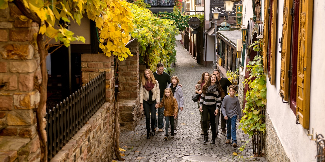 Two families walk up a cobblestone alley flanked by charming buildings