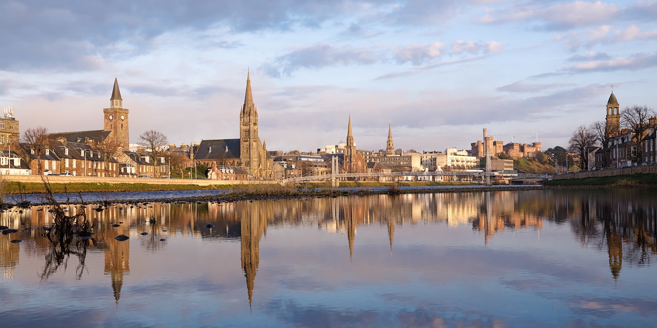 The city of Inverness, with steepled buildings reflected on the water of the River Ness