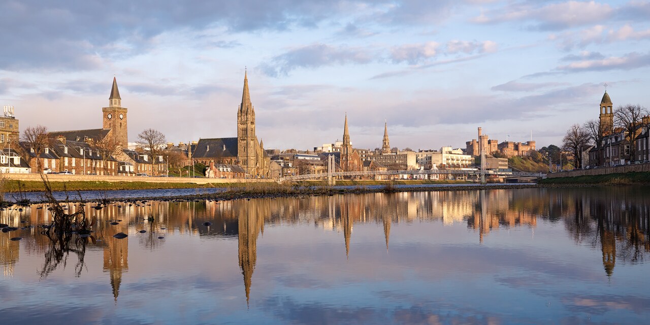 The city of Inverness, with steepled buildings reflected on the water of the River Ness