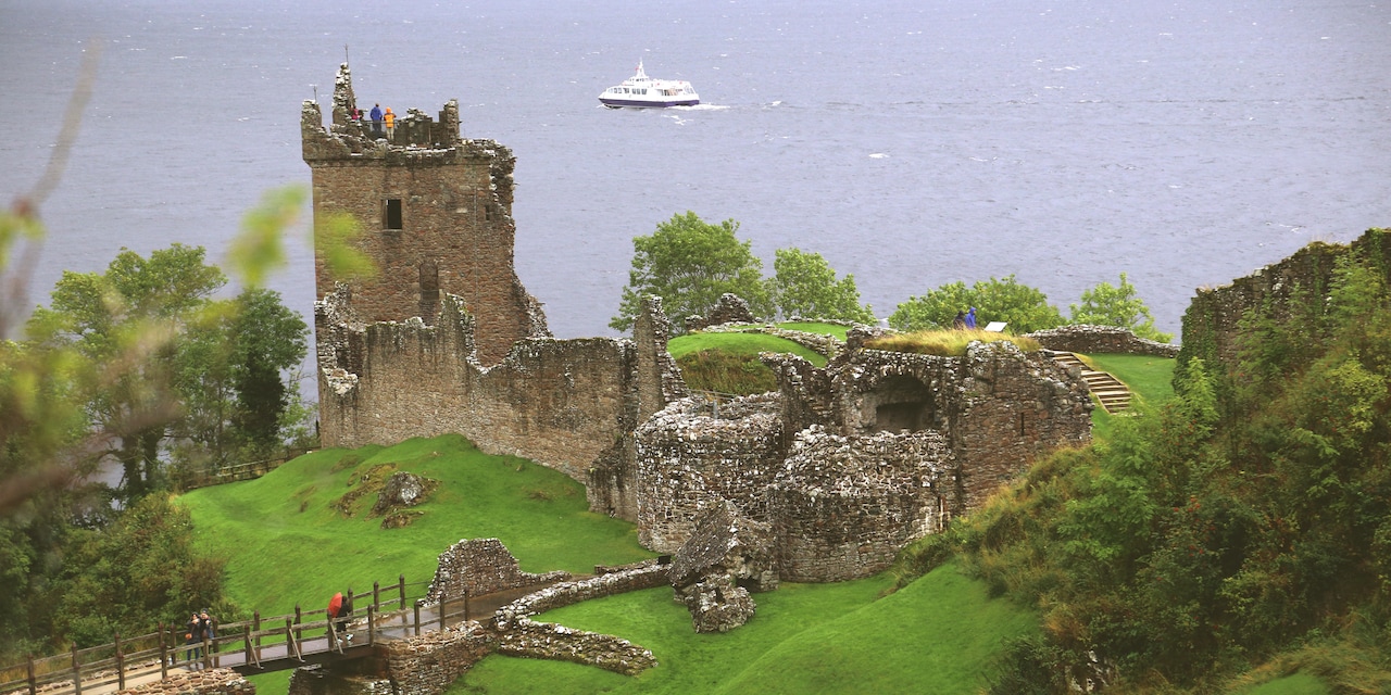 The ruins of Urquhart Castle on a grass covered hill overlooking Loch Ness with a boat in the distance
