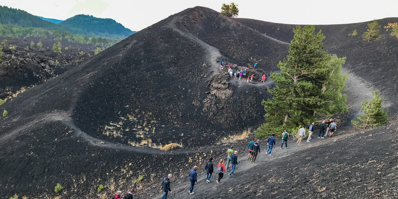 A long line of people walk along a trail on ash-covered Mt. Etna in Sicily