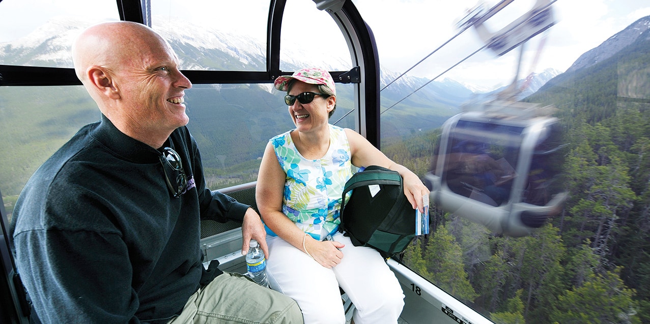 A couple rides a gondola up the side of snowy Sulphur Mountain