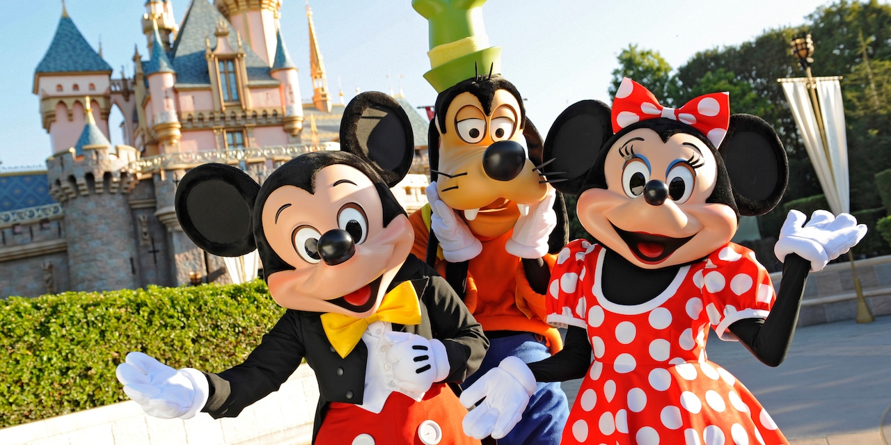 Mickey Mouse, Goofy and Minnie Mouse pose in front of Sleeping Beauty Castle at Disneyland Park