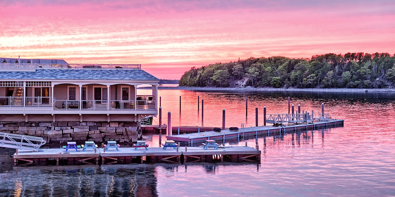 A house on the water in Bar Harbor, Main sits across the lake from a forest-lined river bank at sunset