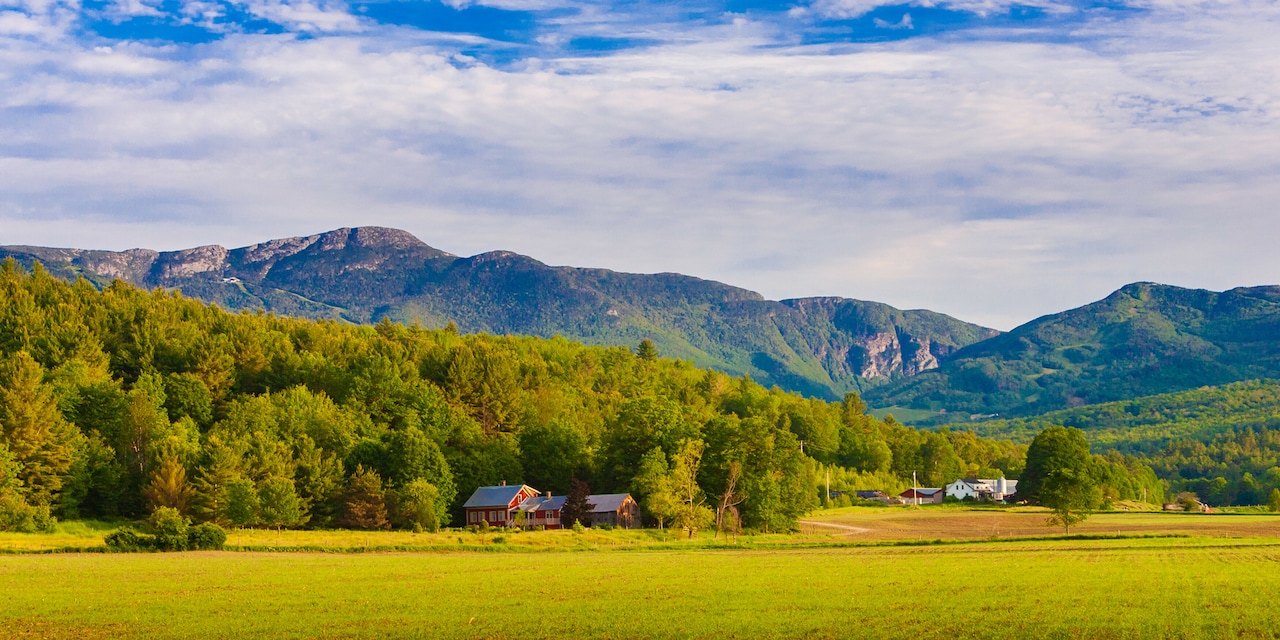 Two New England farms nestled between open fields and lush forest near the base of Mount Mansfield in the background