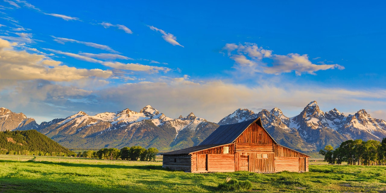 A barn amid a field with snow capped mountains in the background
