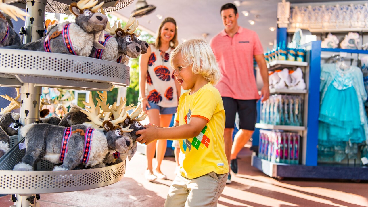 A man and a woman watch at a little boy looking at Sven plush dolls on a store shelf