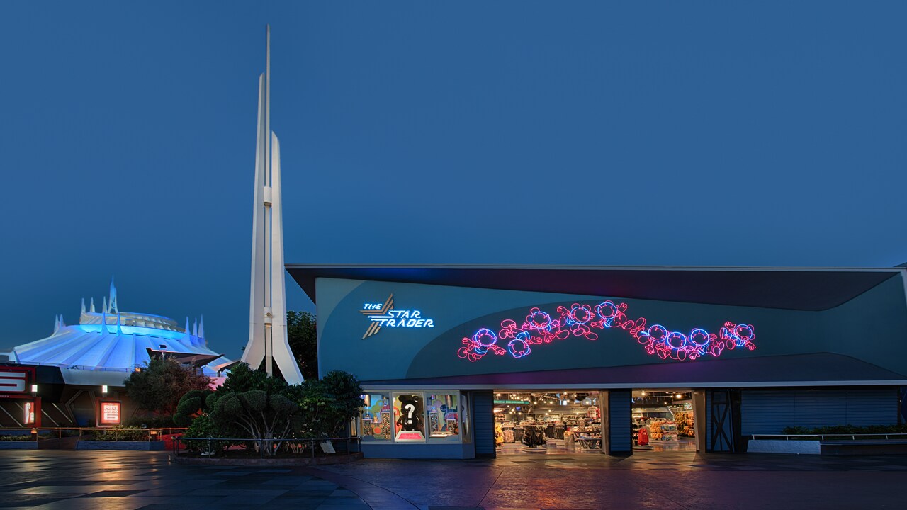 The exterior of Star Trader lights up in evening as spires atop Space Mountain extend toward the sky
