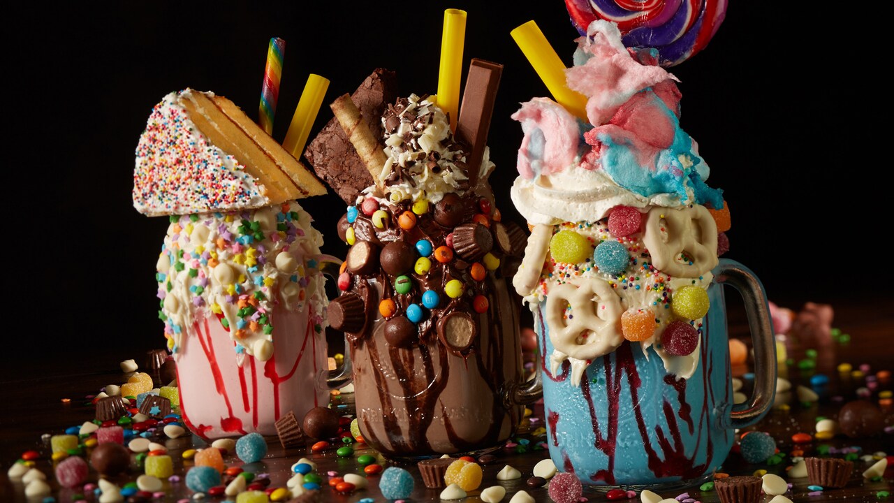 3 large milkshakes topped with assorted candies, cake, cookies and pretzels