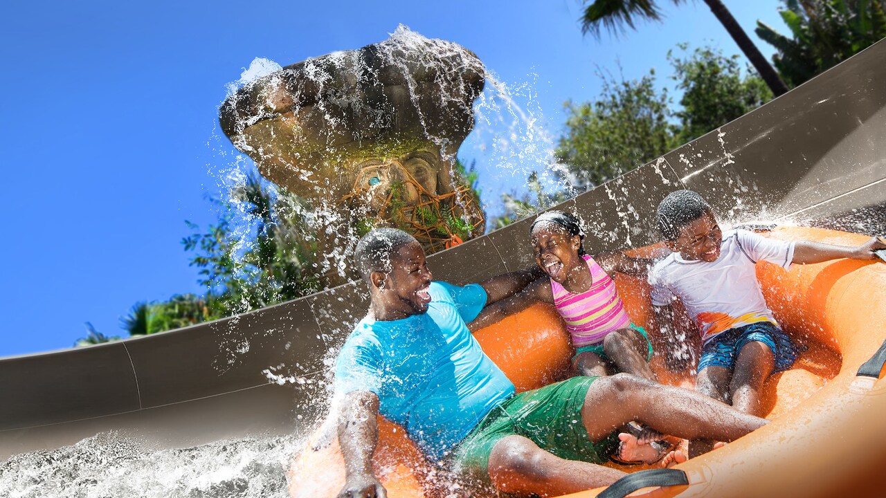 A father, son and daughter get splashed while riding on a family raft at Miss Adventure Falls