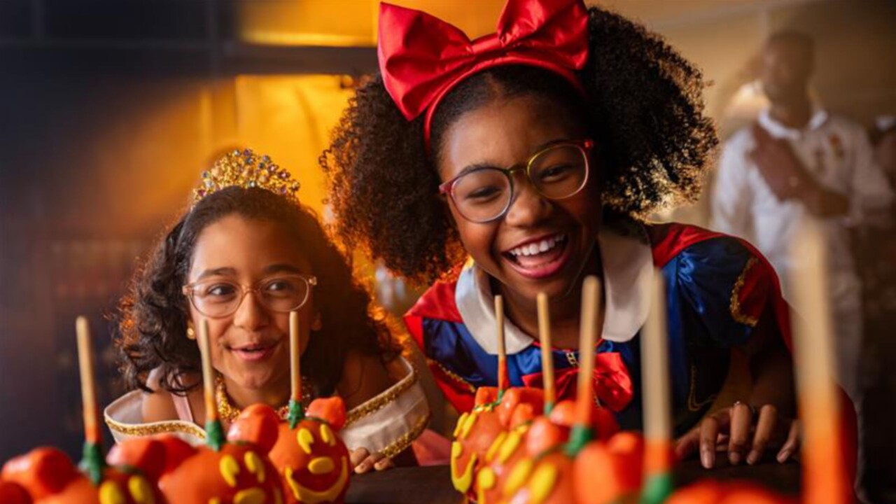 Two girls dressed as Snow White and Aurora looking at Halloween themed Mickey Mouse candy apples