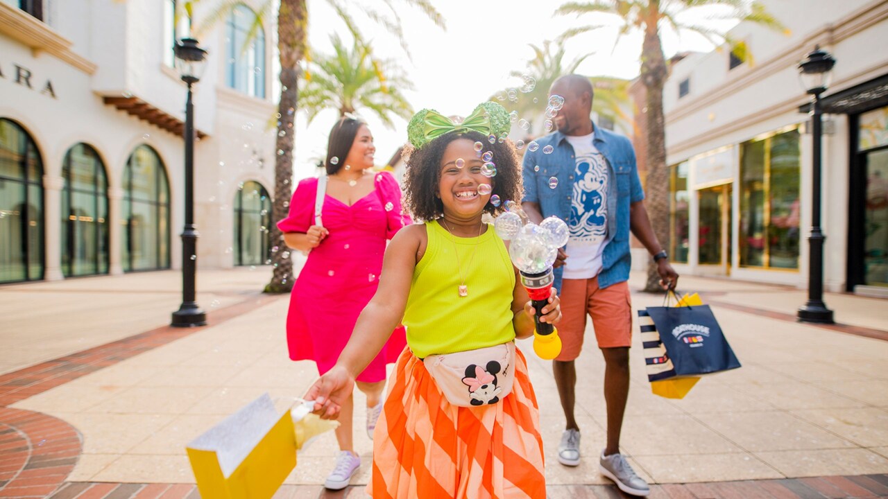 Una niña sonriente con una varita de burbujas pasea por Disney Springs con sus padres