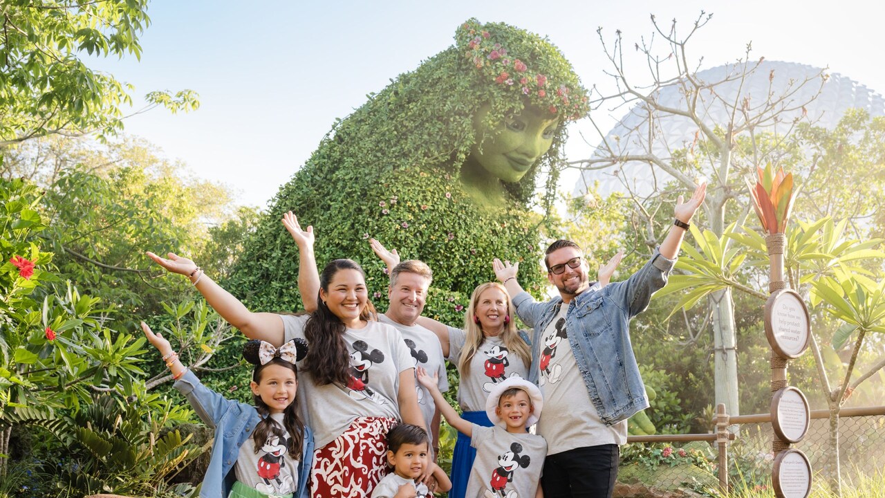 A family of 7 holding their arms up as they pose for a photo in Epcot