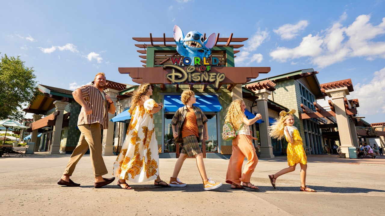 A family of 5 walking in a line in front of the World of Disney retail store at Disney Springs