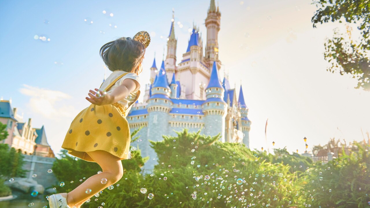A young girl jumping on a grassy lawn near Cinderella Castle at Magic Kingdom park