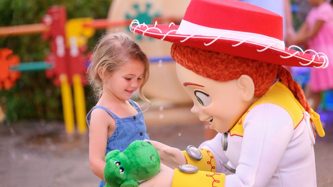 Jessie the Cowgirl crouching down to meet a young girl holding a Rexie toy