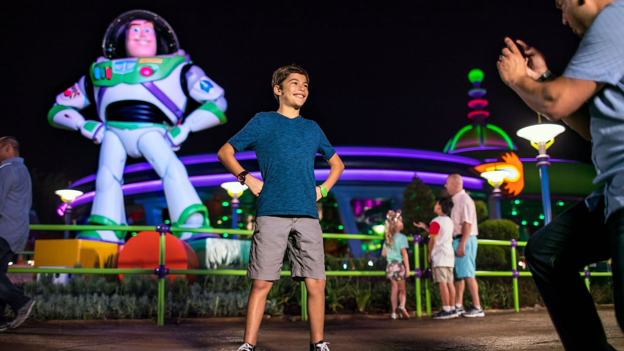A smiling boy poses for his dad taking a photo in front of Buzz Lightyear’s Space Ranger Spin attraction