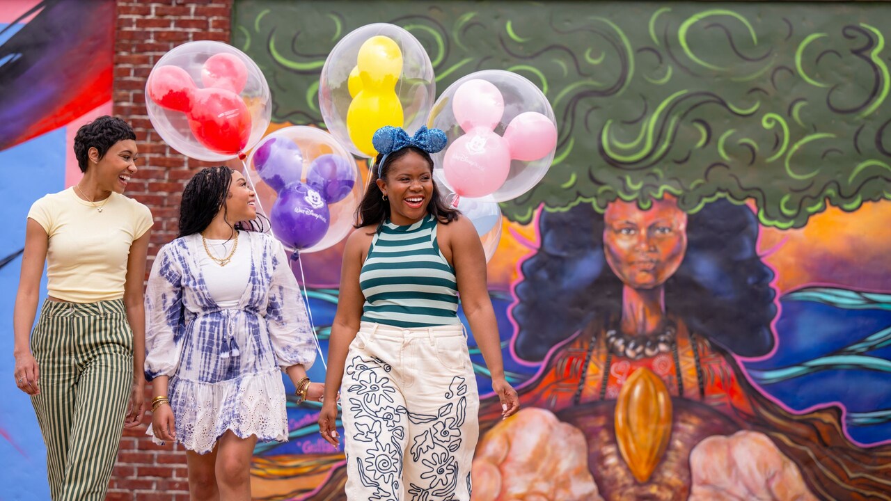 Three Guests holding Mickey Mouse balloons as they walk in front of Disney Springs Art Walk, A Canvas of Expression