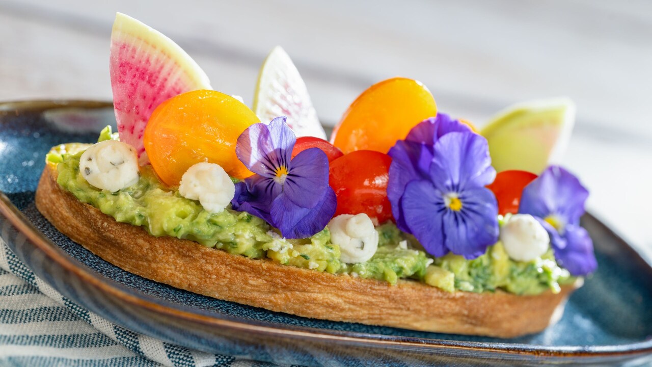 A thick slice of avocado toast topped with grape tomatoes and garnished with fresh flowers