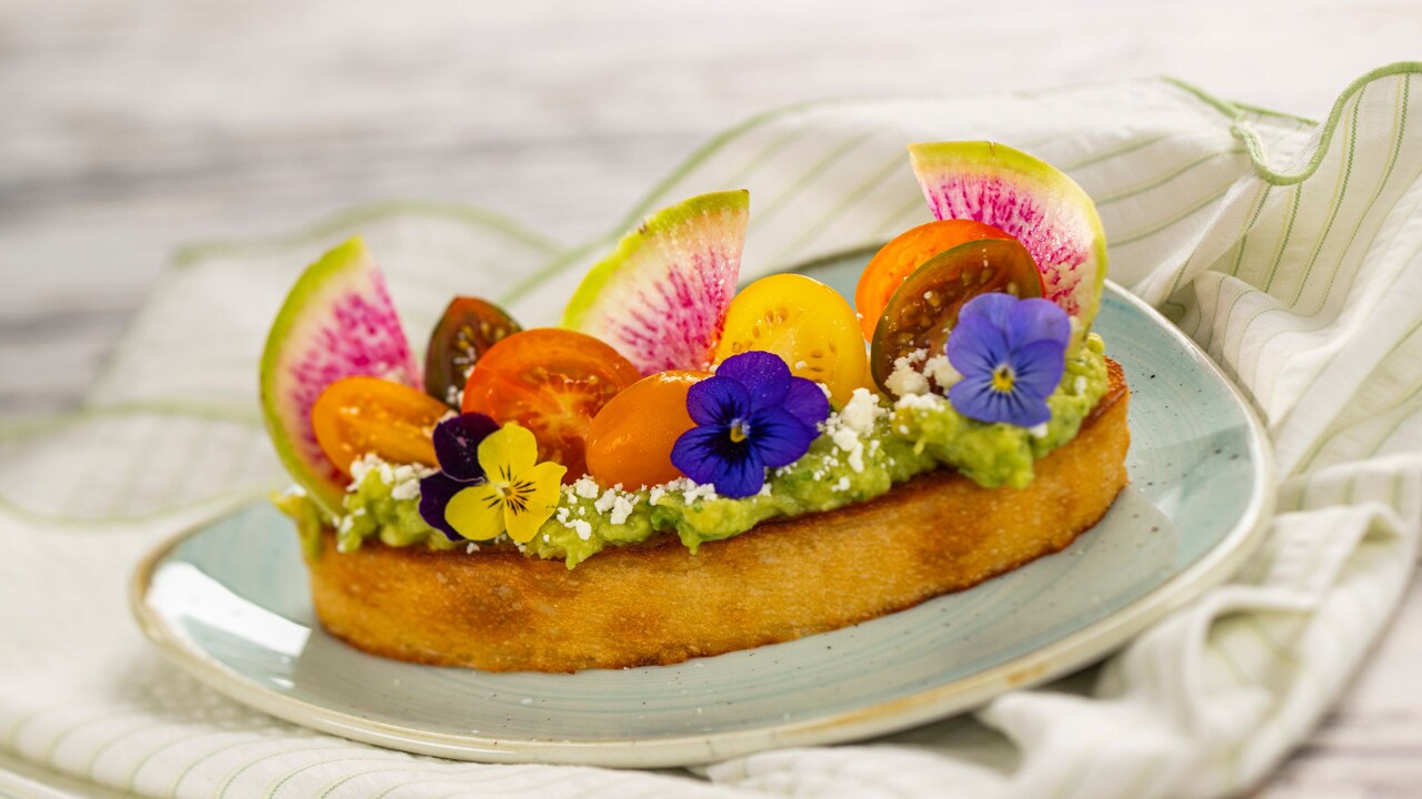 A thick slice of avocado toast topped with grape tomatoes and garnished with fresh flowers 