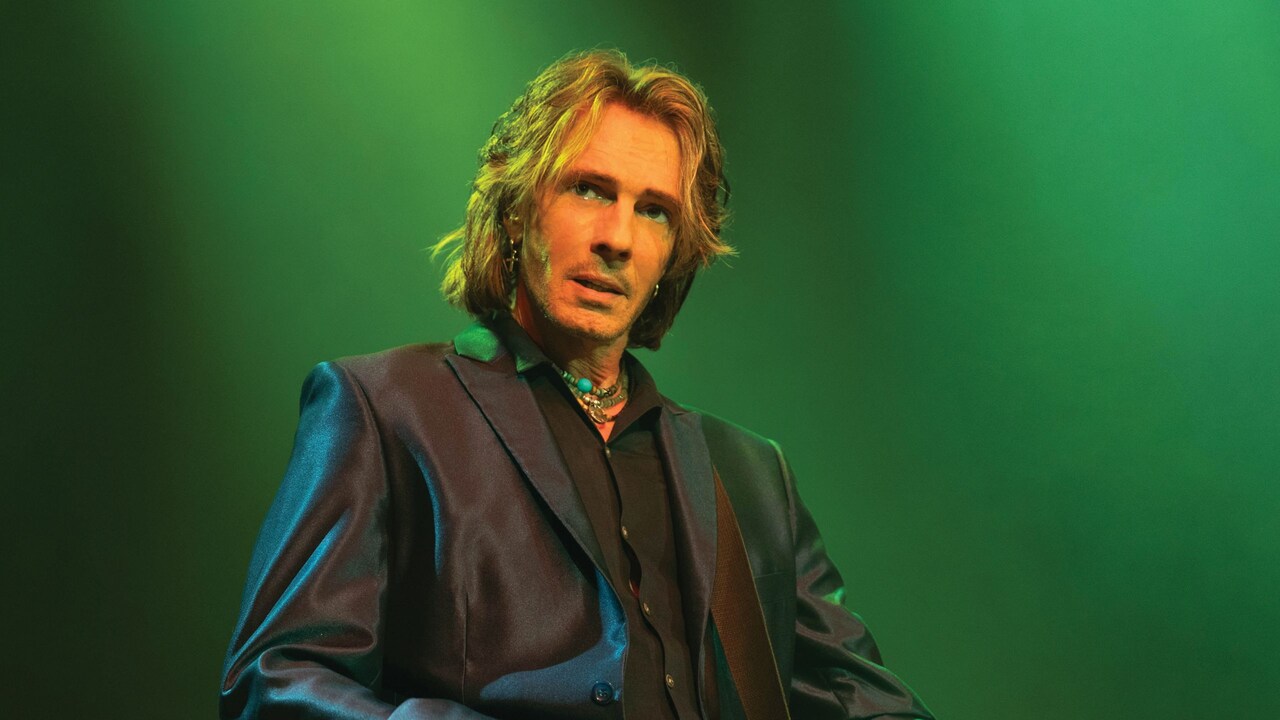 Rick Springfield strumming a guitar while performing on stage