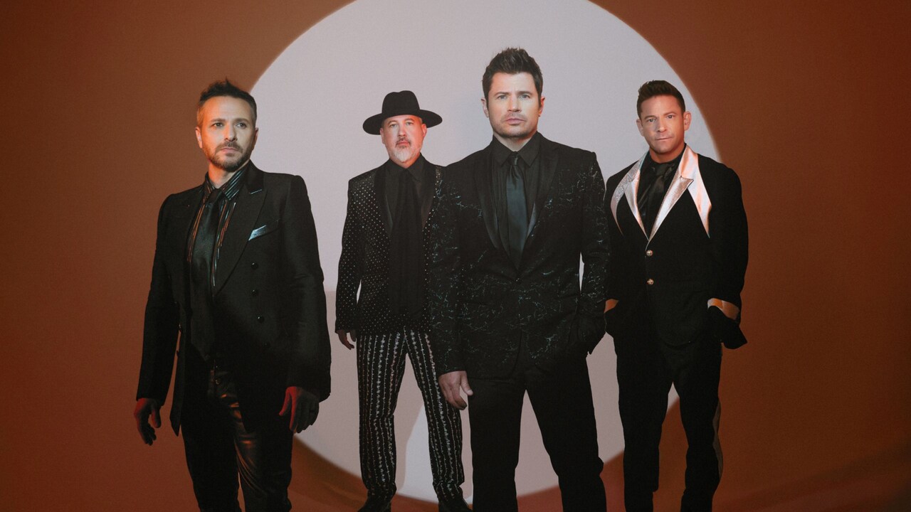 4 members of the group 98 Degrees standing in front of an abstract background