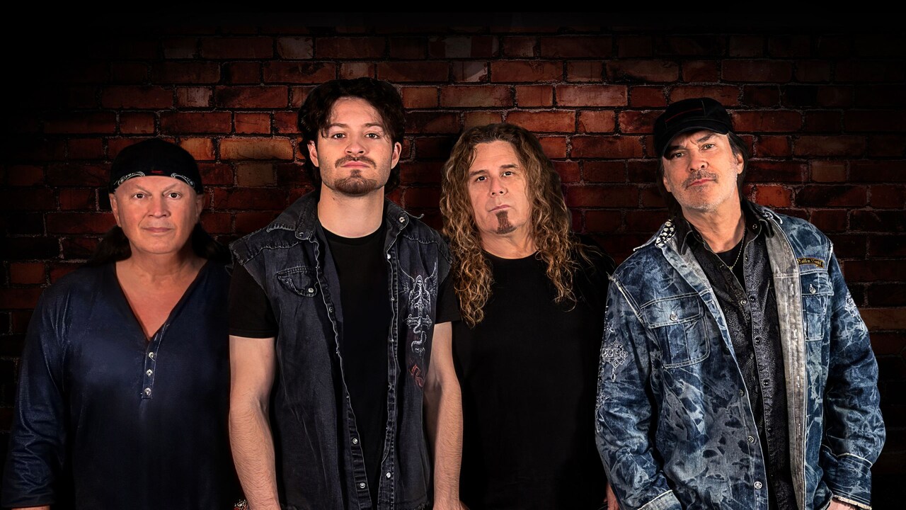 4 members of the band FireHouse standing shoulder to shoulder against a brick wall