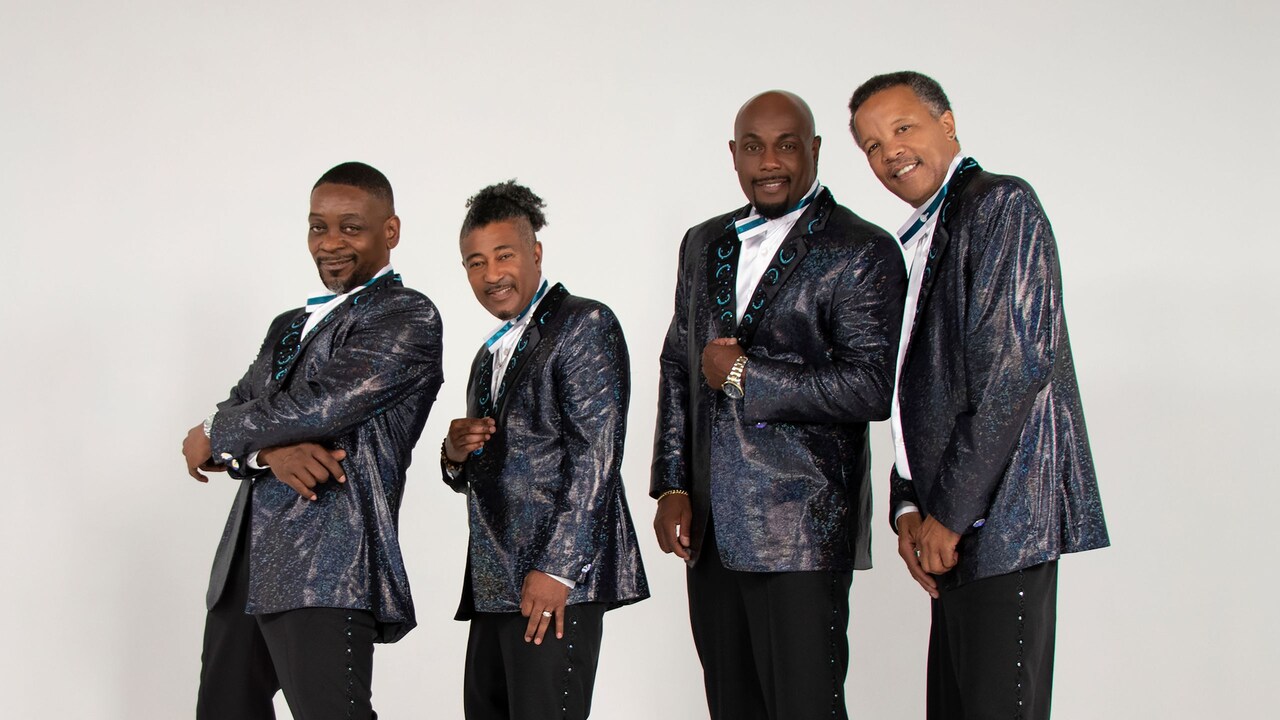 4 members of The Spinners posing together in front of an empty backdrop