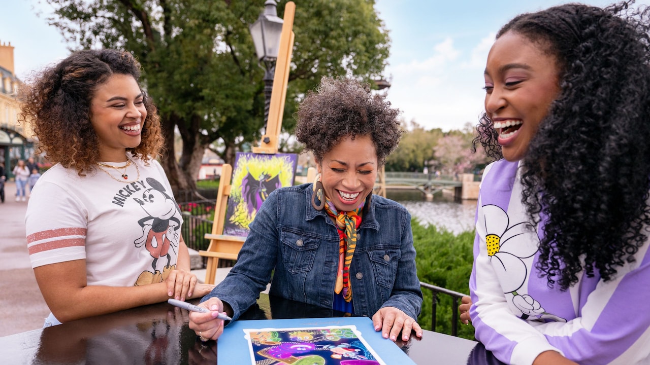 Two Guests smiling while standing next to an artist as she autographs a piece of her artwork at Epcot International Festival of the Arts