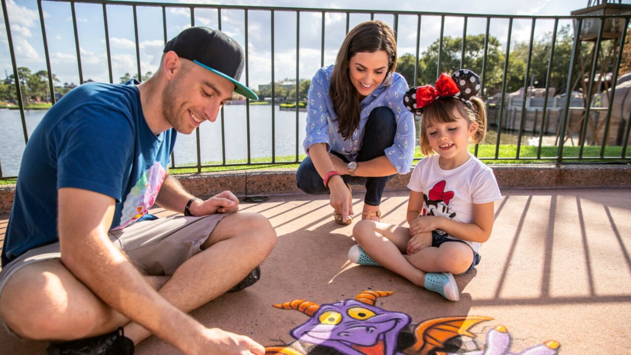 A mother and daughter watch as an artist draws Figment with chalk on the ground at Festival of the Arts