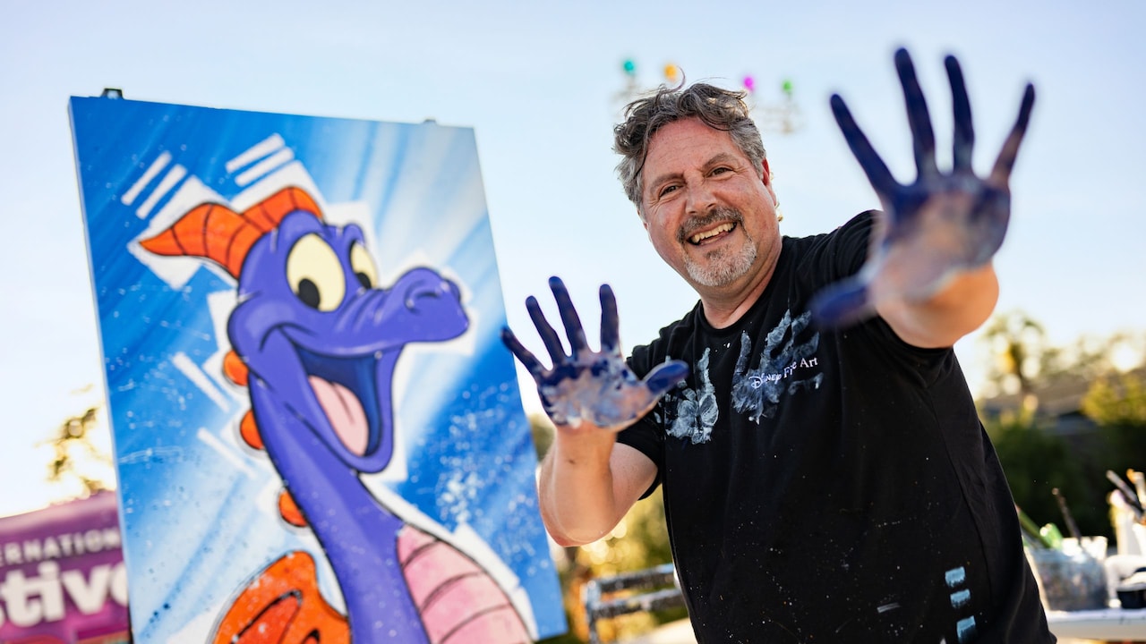 An artist posing next to a painting of Figment during a live Visual Art in Performance demonstration