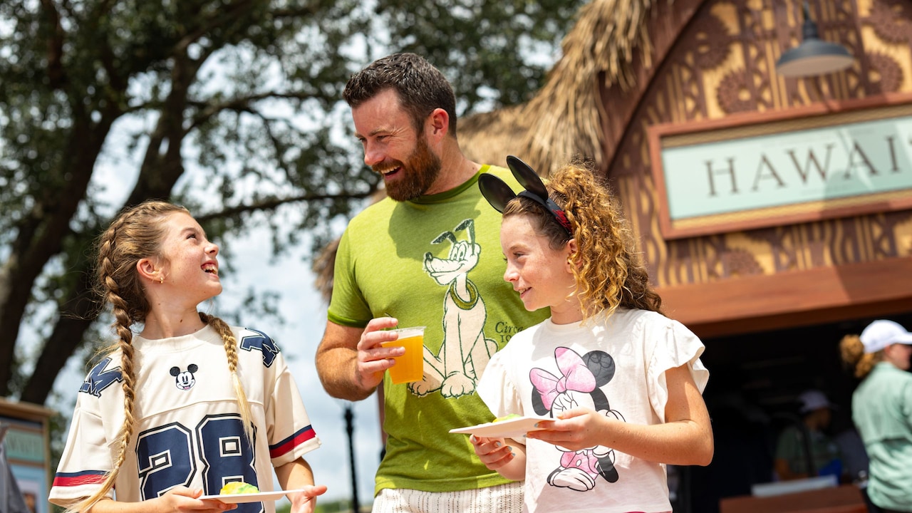 Two young girls and an adult enjoying food and drinks during the Epcot Food and Wine Festival