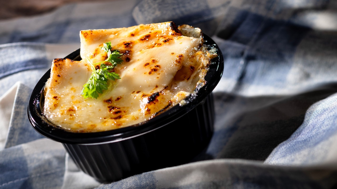 A baked Tartiflette topped with melted, lightly browned Brie cheese, garnished with fresh thyme