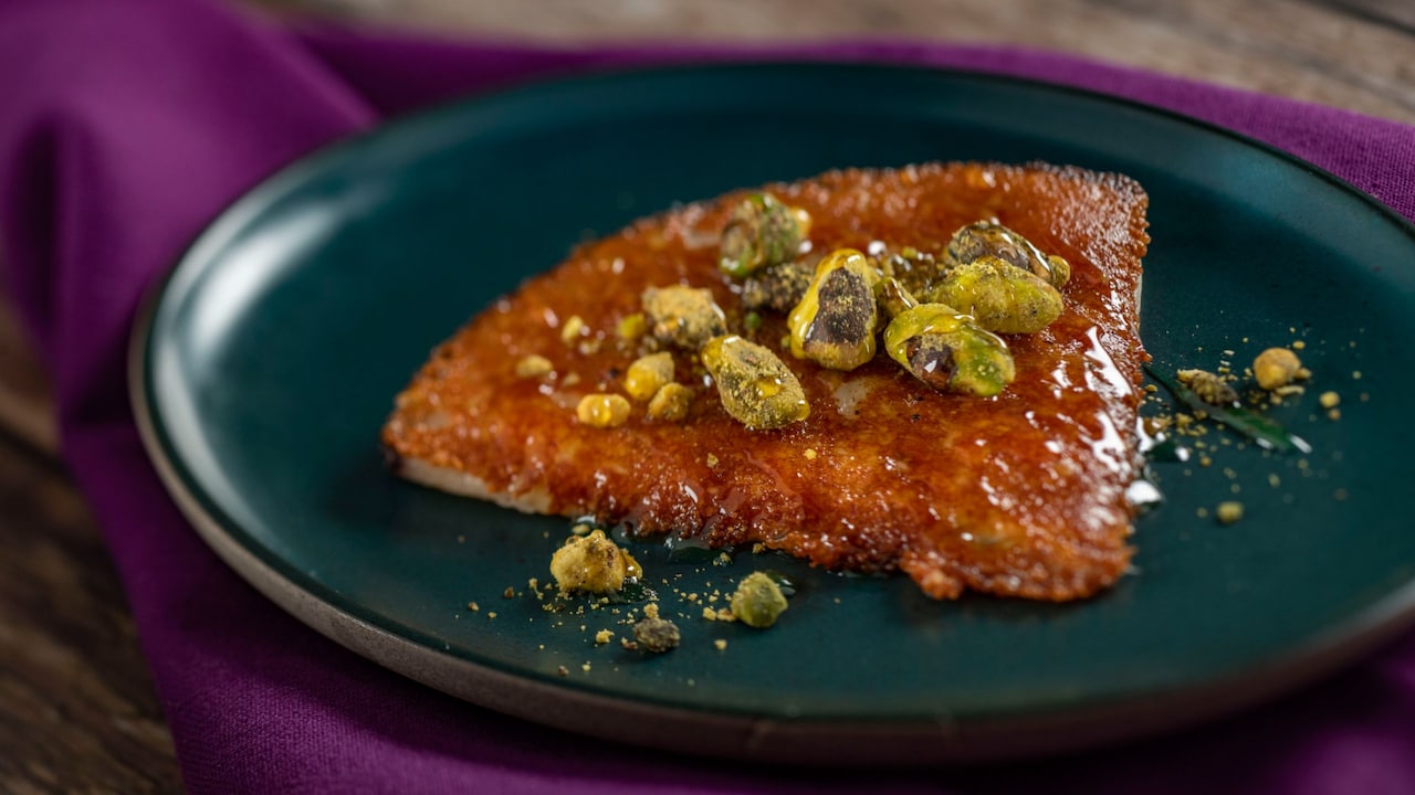A triangular piece of Griddled Cheese topped with pistachios and drizzled with honey