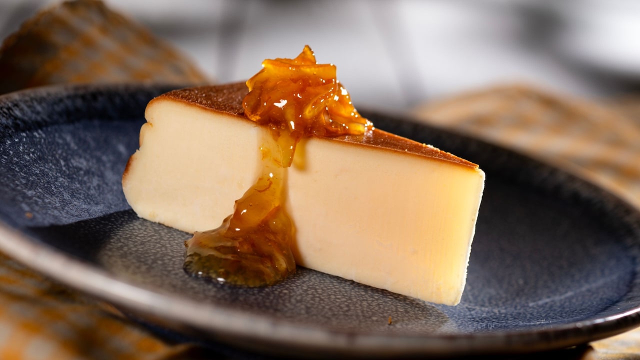 A slice of Basque Cheesecake topped with glossy orange sauce and citrus pieces