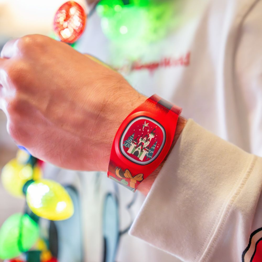 A Guest wearing a Christmas themed MagicBand Plus featuring Cinderella Castle