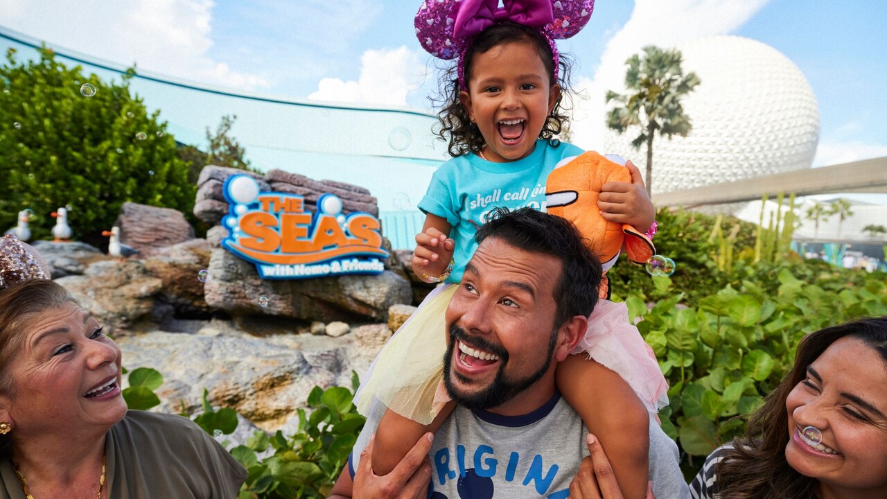 Una joven en los hombros de su padre, con su familia, sonriendo fuera del pabellón The Seas with Nemo and Friends