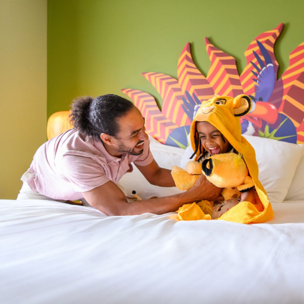 Un père jouant avec un enfant porte un peignoir Simba dans une chambre d’hôtel sur le thème du Roi Lion