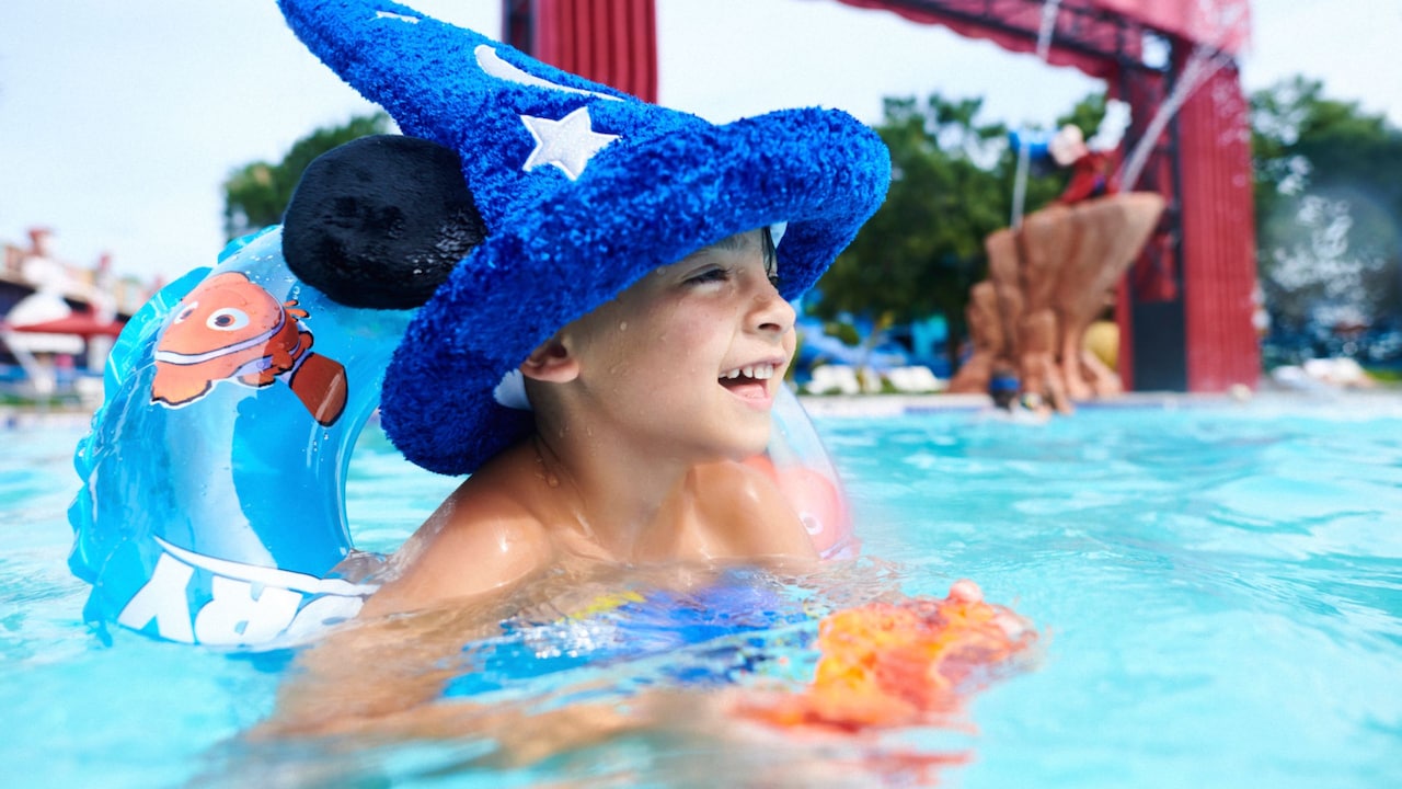 A little boy swims while wearing a Sorcerer Mickey hat