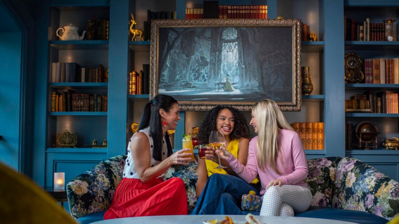 Three friends drink beverages while sitting on a couch in an ornate room