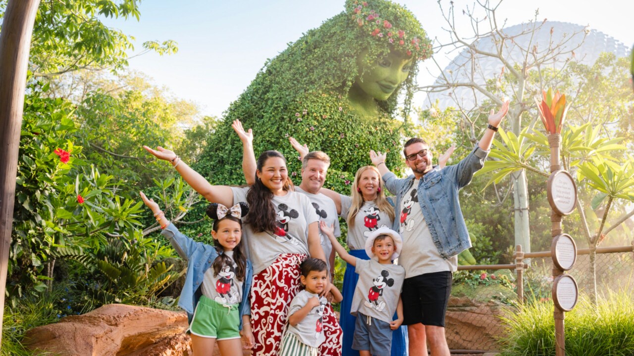 A group of adults and children posing for a photo with their arms in the air in front of Te Fiti at Epcot