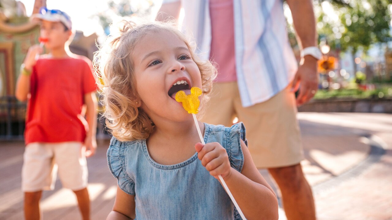 A young girl joyfully eating a Mickey Mouse shaped lolllypop