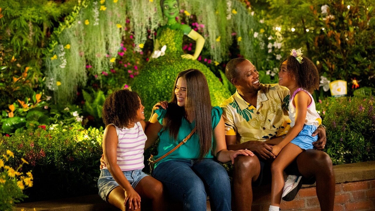 A family of 4 posing with the Princess Tiana Topiary during the Epcot International Flower & Garden Festival