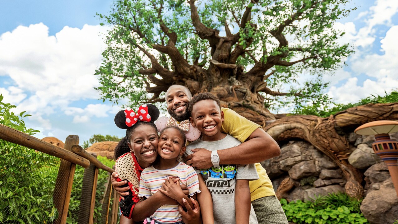  A family of 4 hugging and smiling in front of the Tree of Life at Animal Kingdom theme park