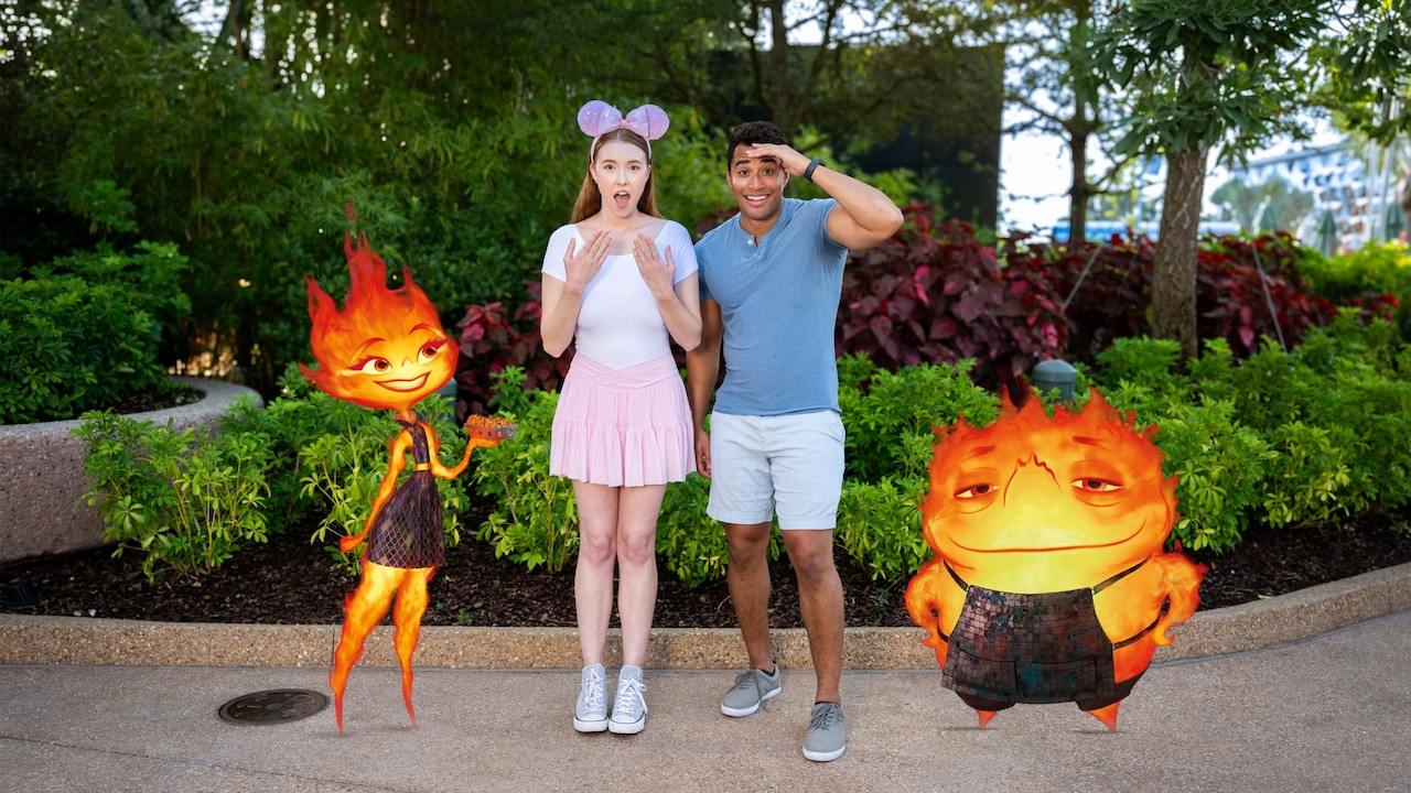A couple at Epcot posing with an augmented reality overlay of Ember Lumen and Bernie Lumen from Elemental