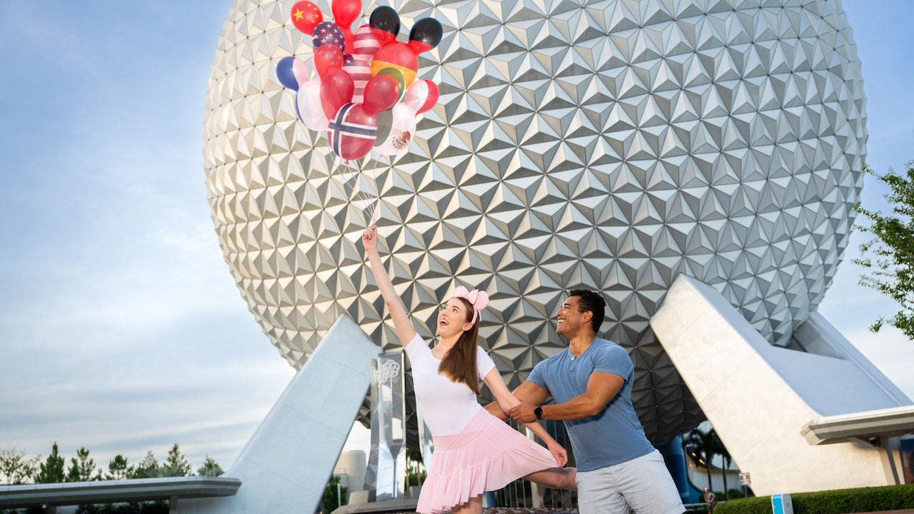 A couple holding a bunch of augmented reality balloons featuring the flags of various countries in front of Spaceship Earth at Epcot