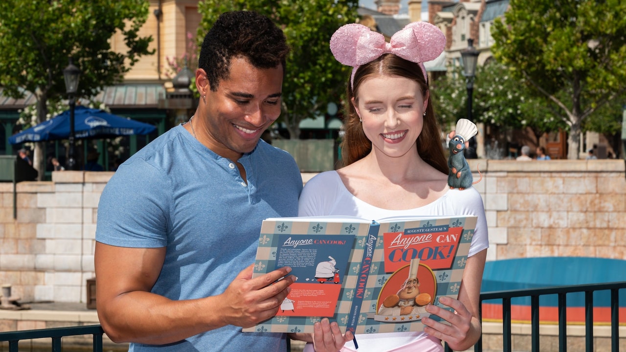 A couple at Epcot posing with an augmented reality overlay of a cookbook and Remy from Ratatouille